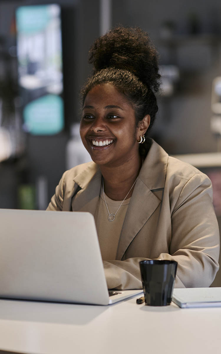 Hymyilevä nainen istuu kahvilassa tietokoneen äärellä.