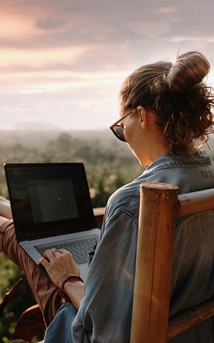 Nainen istuu ulkona terassilla ja käyttää kannettavaa tietokonetta.
