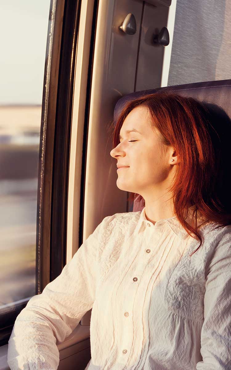 Nainen matkustaa junassa silmät kiinni nauttien auringosta.